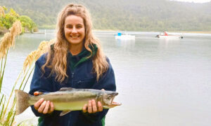 Smiling woman holding a trout in front of a lake