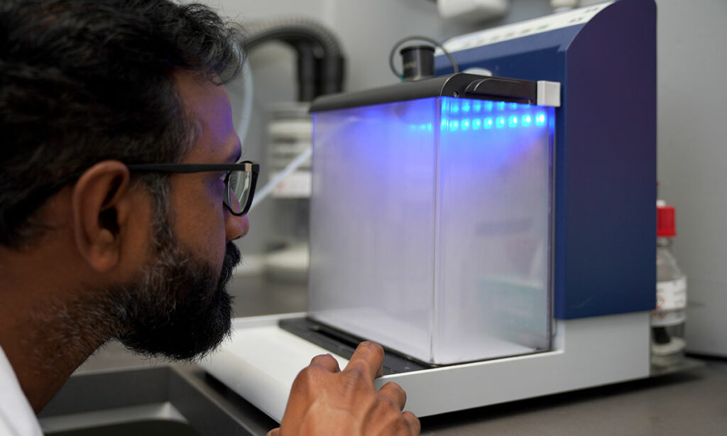 Laboratory technician watches sample being analysed in machine